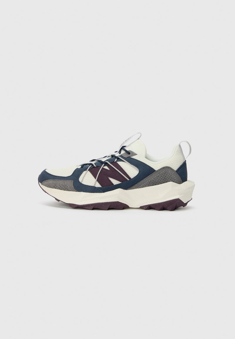 Sneakers featuring a cream mesh upper, navy and gray suede overlays, purple rubber outsole, and reflective detailing on the laces.