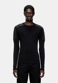 Pull noir à côtes avec des manches longues, présentant des accents d'épaule en cuir. Design ajusté, texture lisse, col rond. Pantalon noir.