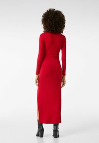 Abito maxi a coste rosso con maniche lunghe, caratterizzato da uno spacco laterale, design aderente e abbinato a stivali neri con tacco a blocco.
