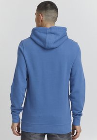 Sudadera con capucha azul, de mangas largas y con un tejido texturizado. Presenta una capucha grande y un dobladillo recto a la altura de la cintura.