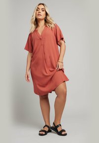 Rostfärgad, kortärmad klänning med v-ringning, har en avslappnad passform och mjuk textur, i kombination med svarta sandaler.