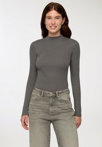 Szara, długorękawowa bluzka z wysokim kołnierzem, wykonana z prążkowanego materiału, w połączeniu z jasnymi, wyblakłymi dżinsami z wysokim stanem i zapięciem na guzik z przodu.