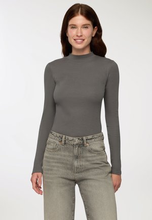 Top grigio a maniche lunghe con colletto alto realizzato in tessuto a coste, abbinato a jeans chiari scoloriti con alta vita e chiusura con bottoni frontali.