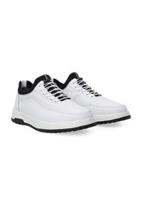 White sneakers with a textured mesh upper, black accents around the collar, and white laces. Thick black rubber sole with stitching detail.