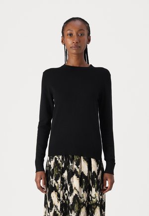Black long-sleeve sweater in a fitted design, made from soft knit fabric. Ribbed cuffs and hem. Paired with a patterned long skirt.