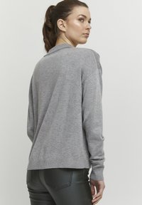 Lys grå sweater i blødt strikkemateriale, med rund hals og ribbede manchetter. Stylet med en afslappet pasform og minimal detaljer.