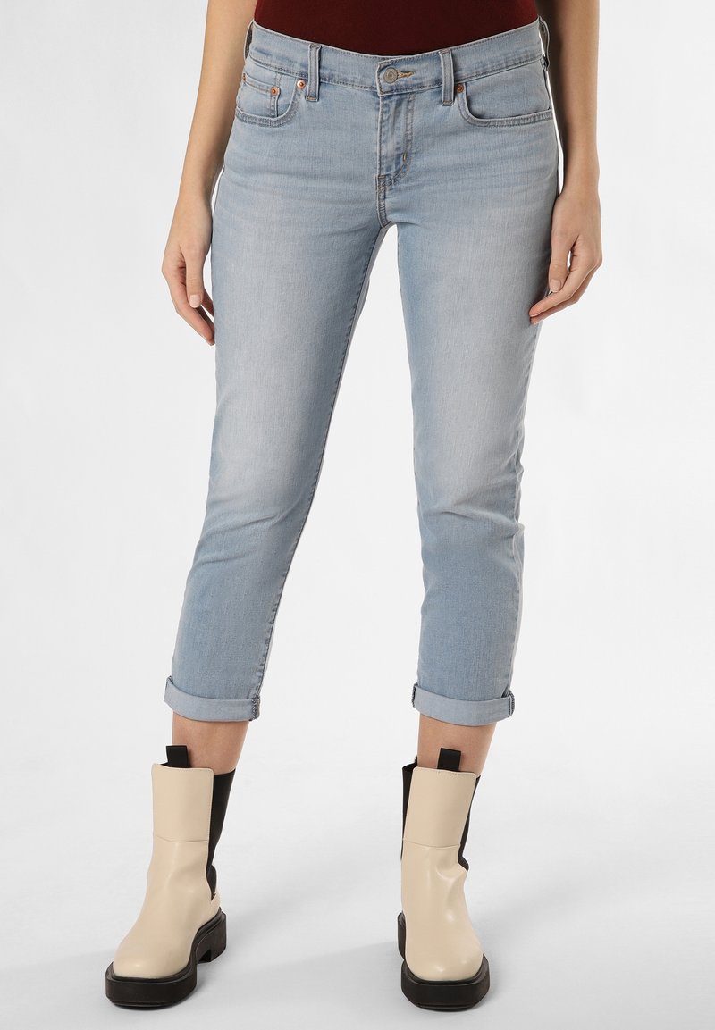 Světlé modré džíny s úzkým střihem, vyhrnuté nohavice, pět kapes a měděné detaily, spárované s krémovými kotníkovými botami s černými akcenty.