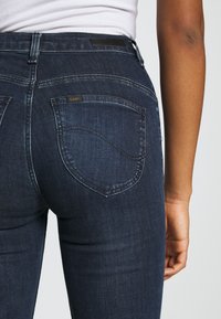 Mörkblå denimjeans med en figurnära silhuett, som har två bakfickor, en liten "Lee"-logotag och subtila sömdetaljer.
