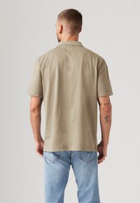 Kortermet, olivengrønn skjorte laget av myk stoff, med enkel design, rett kant og krage, brukt sammen med lyseblå jeans.