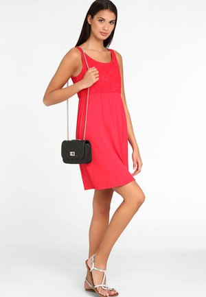 Robe sans manches rouge avec des détails en dentelle au niveau du buste, tissu léger, coupe ample, assortie à des sandales argentées et un petit sac à bandoulière noir.