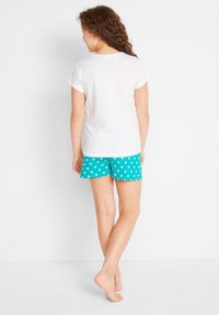 T-shirt en coton blanc avec des manches roulées associé à un short turquoise à pois. Le short a une coupe décontractée et une texture douce.