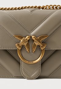 Borsa a tracolla in pelle beige con design trapuntato. Presenta una chiusura con motivo di uccello in tono oro e una tracolla a catena. Forma rettangolare con dettagli arrotondati.