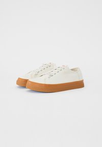 White canvas shoes with a textured rubber sole. Features round laces and small eyelets. The sole is brown with a ridged pattern.