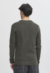 Grønn strikket genser med rund hals, lange ermer og ribbestrikkede mansjetter. Myk tekstur, tettsittende silhuett og ensfarget design.