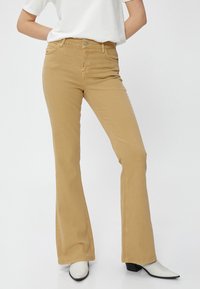 Beige Schlagjeans aus Baumwolle, mit einer Vorderseite, Knopfverschluss und einer glatten, leicht strukturierten Oberfläche.