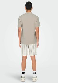 Herre polo med kortærmer i lysegrå stof, parret med stribede shorts. Funktioner omfatter en klassisk krave og kontrasterende sokker med striber.