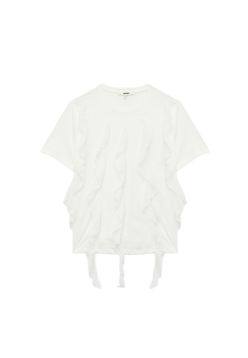 Camiseta blanca de manga corta con volantes en capas a lo largo de los lados frontales y lazos en el dobladillo inferior. Tejido suave, corte relajado.