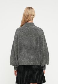 Pelēks, pūkains džemperis ar augstu apkakli un brīvu piegriezumu, ar garām piedurknēm. Saskaņots ar melnu ieplestu svārku ar baltām svītrām.