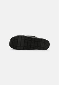 Semelle de chaussure en caoutchouc noir avec un motif de prise texturé. Présente un logo circulaire et une forme plate et arrondie.