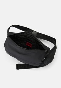 Sacoche HUGO noire avec sangle ajustable, fermeture éclair supérieure, patch logo rouge intérieur et plusieurs compartiments intérieurs, présentée ouverte sur fond blanc.