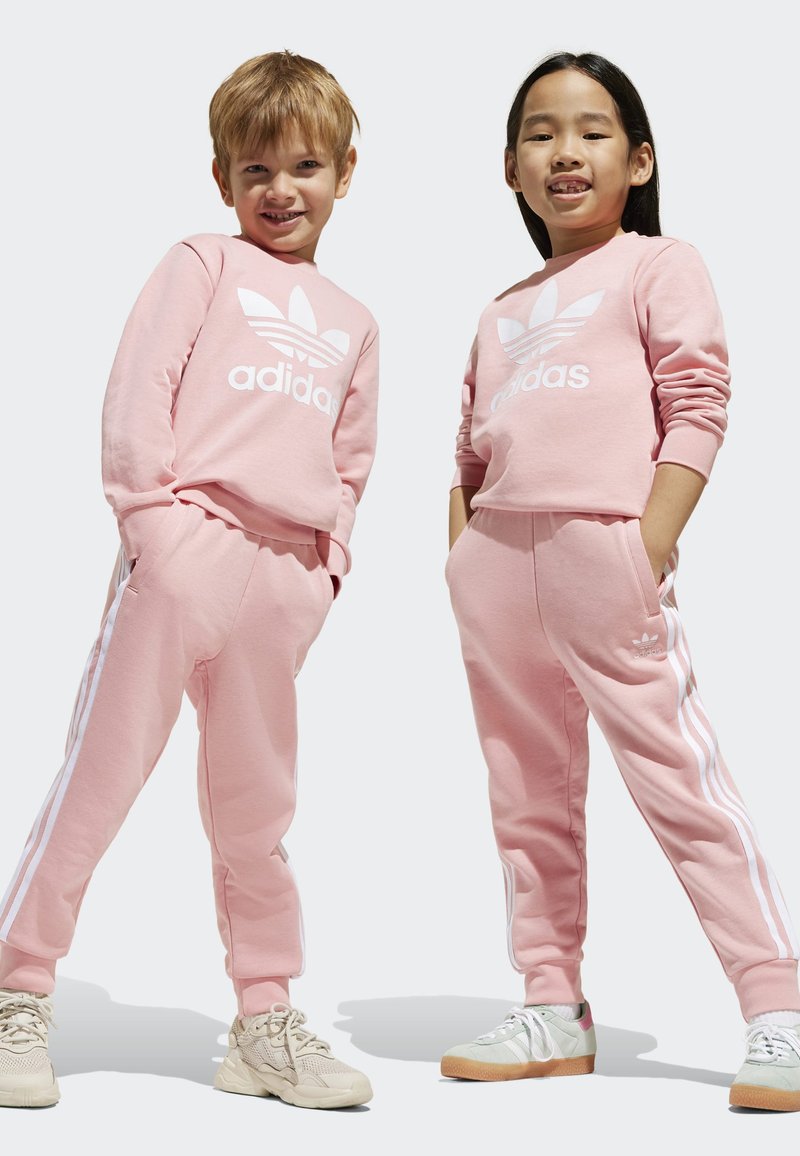 Ružové bavlnené mikiny a nohavice s bielym logom Adidas a pruhmi. Textúrovaná látka; pružné manžety; ľahké topánky v béžovej a zelenej farbe.