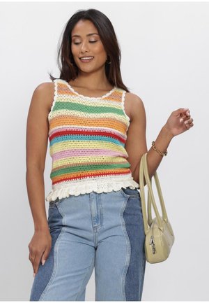 Vrouw draagt een meerkleurig gestreept gehaakt tanktopje, tweekleurige high-waisted jeans en houdt een lichtgele handtas vast op een witte achtergrond.