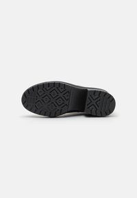 Black rubber shoe sole with a textured surface featuring a geometric pattern for grip, showing curves at the edges and a reinforced heel section.