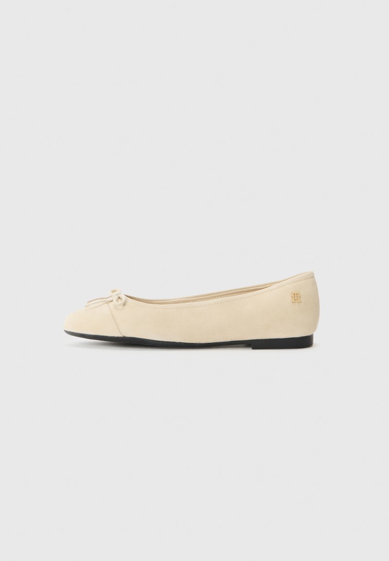 Chaussure ballerine de couleur crème avec un petit nœud sur le devant et une semelle noire, vue de profil sur un fond clair.