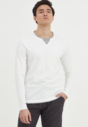 Long-sleeve white T-shirt featuring a V-neck with gray inner lining, paired with dark pants. Smooth fabric, casual fit, minimal design.