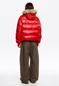 Czerwona puchowa kurtka ze ściąganym kapturem wykończonym futerkiem, zaprojektowana w krótkim, pudełkowym kroju. Połączona z luźnymi, szerokimi oliwkowymi spodniami.