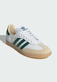 Sneaker Adidas Samba bianco con strisce verdi, punta in morbido camoscio e suola in gomma. Inclusi lacci e colletto imbottito.
