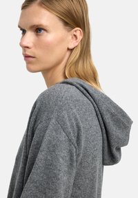 Szara bluza z kapturem, wykonana z miękkiej dzianiny, charakteryzująca się prostym designem, dużym kapturem i luźnym krojem. Delikatna tekstura i brak widocznych wzorów.