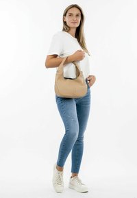 Sac hobo en cuir beige de forme arrondie, avec une seule anse et des détails de couture subtils, présenté sur un fond blanc.