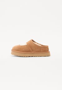Brune suede slip-on sko med lammepelsfôr, lav hæl og teksturert gummisåle. Har en rund tå og minimale sømdetaljer.