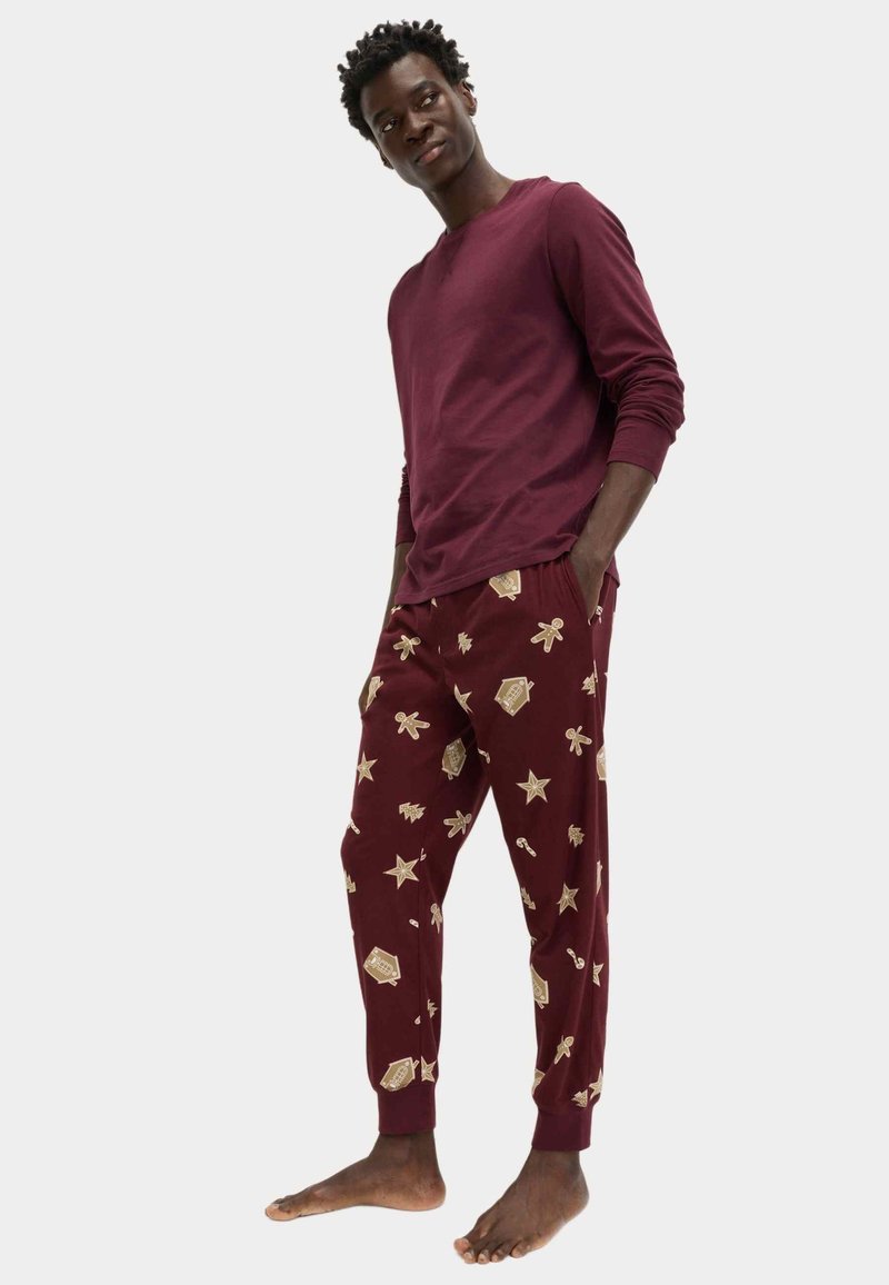 Camisa de manga larga burdeos combinada con pantalones burdeos que presentan patrones de oro con temática navideña, incluyendo estrellas y pan de jengibre, de corte relajado.