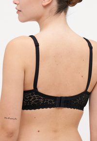 Melna mežģīņu bralette ar regulējamām siksnām, viļņotu malu un aizmugurē esošu āķa un acs aizdari ar delikātu rakstu.