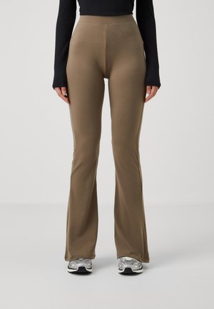 Pantalons évasés en tissu brun neutre, présentant une texture lisse et une taille haute, associés à des chaussures de sport grises.