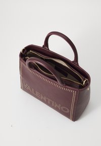 Burgunderfarbene Ledertasche mit Nietenverzierungen, zwei oberen Tragegriffen und einem geräumigen Innenraum mit Reißverschlusstaschen.