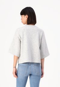 Šedý oversized svetr s krátkými rukávy, měkkou texturou a kulatým výstřihem, spárovaný s světle modrými slim jeans. Jednoduchý, uvolněný design.