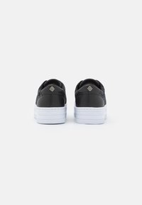 Baskets noires avec une tige texturée, des accents en cuir, une semelle épaisse blanche et un détail de marque en or au talon.