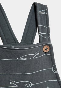 Graue overall mit weißen Linienzeichnungen von Tieren, ausgestattet mit verstellbaren Trägern und einem Holzknopfdetail am Verschluss.