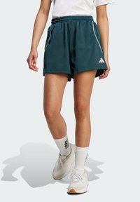 Tyrkysové sportovní šortky s bílými bočními pruhy, vyrobené z lehké látky. Mají elastický pas a jsou nošeny s bílými ponožkami a teniskami.