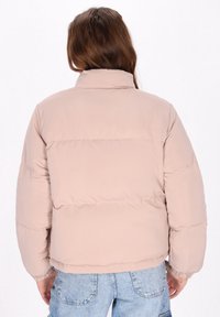 Chaqueta de pluma beige claro con un cuello alto, puños elásticos y costuras horizontales. El material parece suave y acolchado.