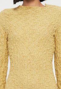 Κίτρινο φόρεμα με υφή και μακριά μανίκια, με υλικό ρυτιδωμένο και ψηλό, στρογγυλό λαιμόκοψη.