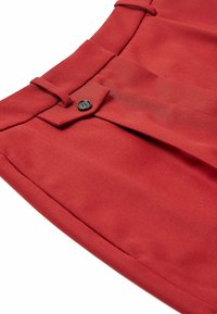 Pantalon en tissu rouge à texture lisse, doté d'un pli latéral, d'une fermeture à bouton et de détails cousus à la taille.