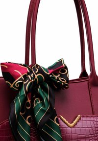 Burgundská kabelka s hladkými a texturovanými částmi, ozdobená černým a červeným hedvábným šátkem se zelenými a zlatými vzory uvázaným na mašli.