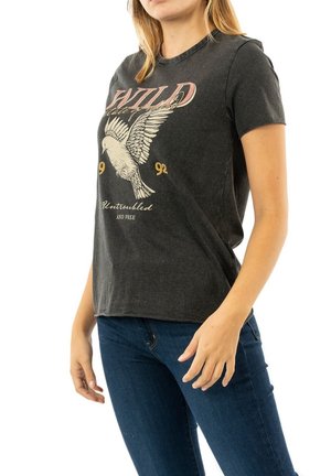 Femme portant un T-shirt noir avec un graphisme d'oiseau en vol et le texte « WILD 92 Untroubled and free » associé à un jean bleu foncé.