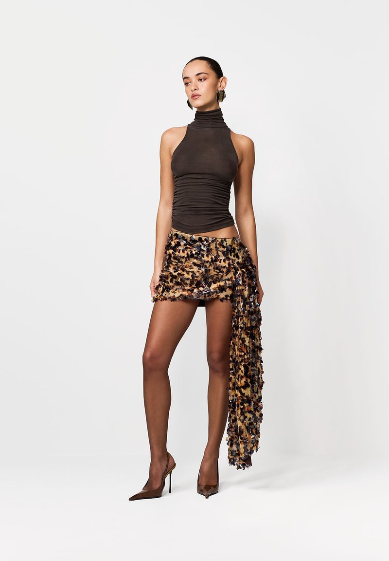 Brązowy top bez rękawów z wysokim kołnierzem, zestawiony z mini spódnicą w panterkę z falbankami, noszony z brązowymi szpilkami.
