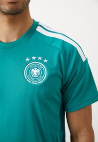 Camisola desportiva azul-petróleo com riscas brancas, apresentando o logo bordado da Associação Alemã de Futebol e quatro estrelas acima dele.