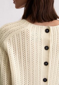 Cremefarbener Strickcardigan mit einem strukturierten Muster, vertikalen Streifen und schwarzen Knöpfen auf der Rückseite für den Verschluss.